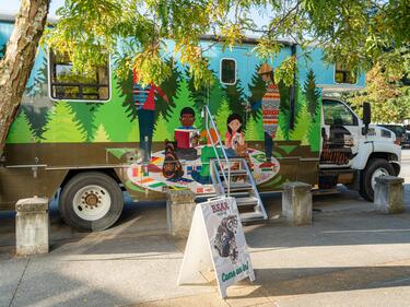 Decorated RV bus parked, with a sandwich board sign sitting out that reads "Bear Bus"