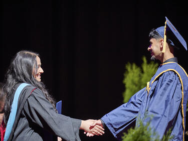 Graduating student in regalia shaking hands with an administrator at a graduation