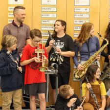 Group of students holding new instruments. Adult looks on at them.